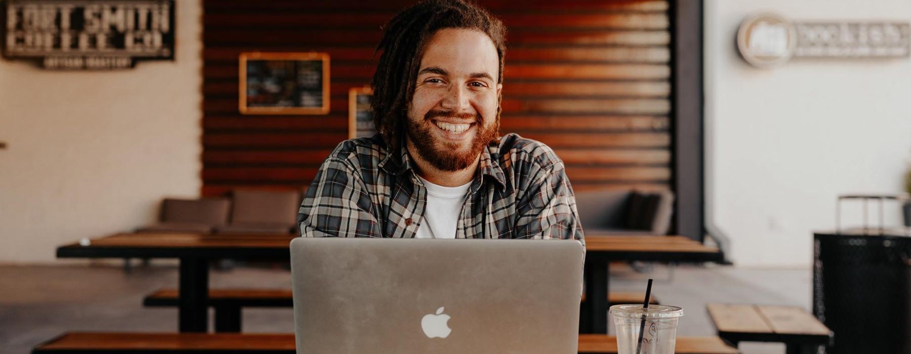 man sits with a drink in front of an open laptop in local restaurant